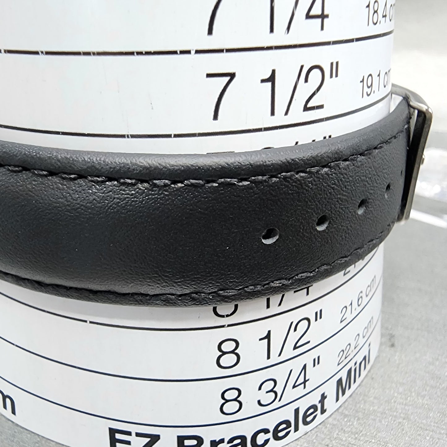 Black leather watch band on bracelet size measuring cylinder with size chart visible