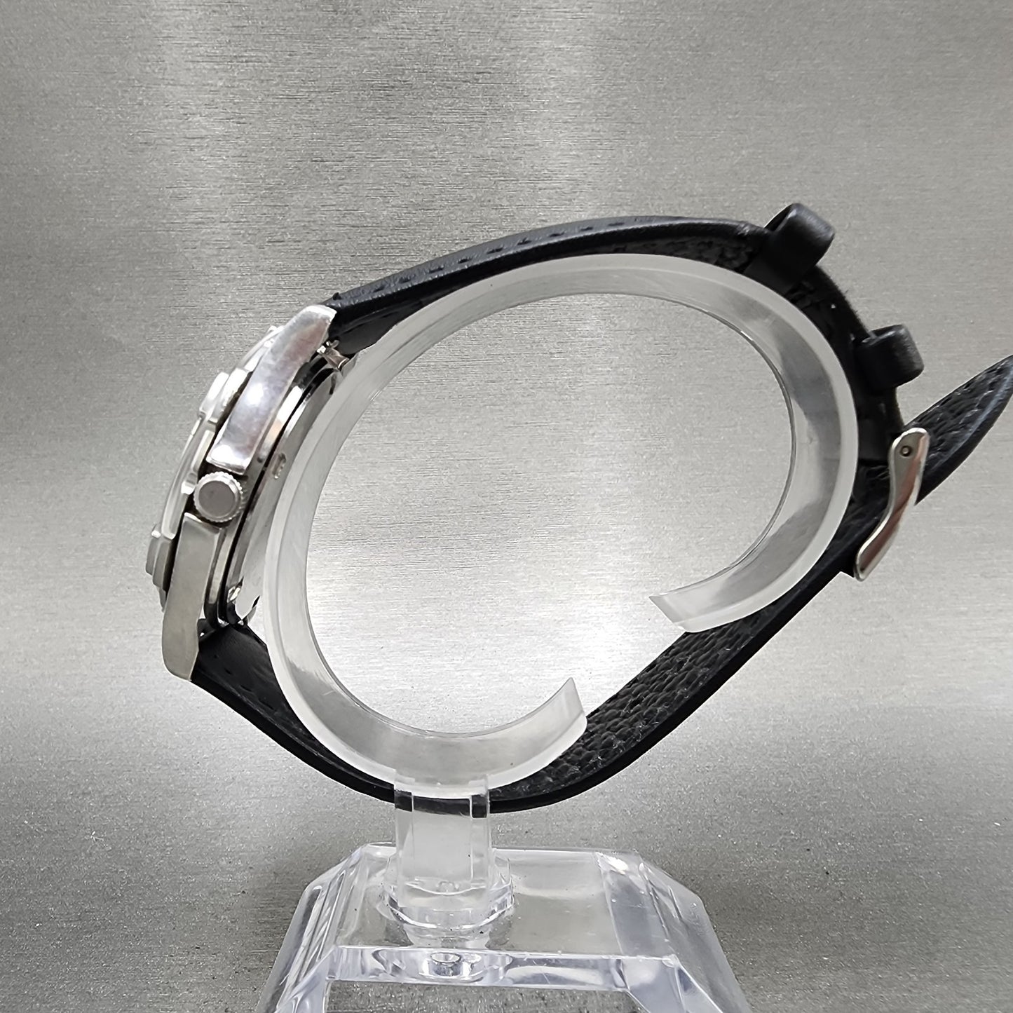 Side view of stainless steel chronograph watch with black textured leather strap on display stand