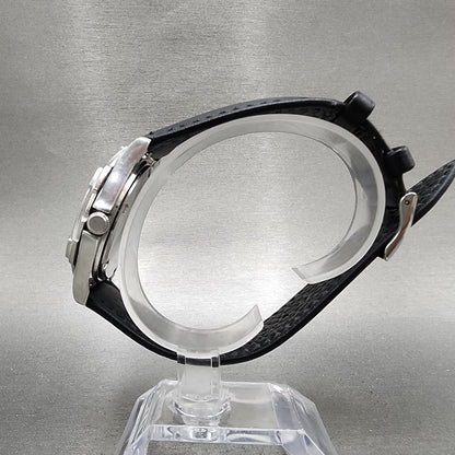 Side view of stainless steel chronograph watch with black textured leather strap on display stand
