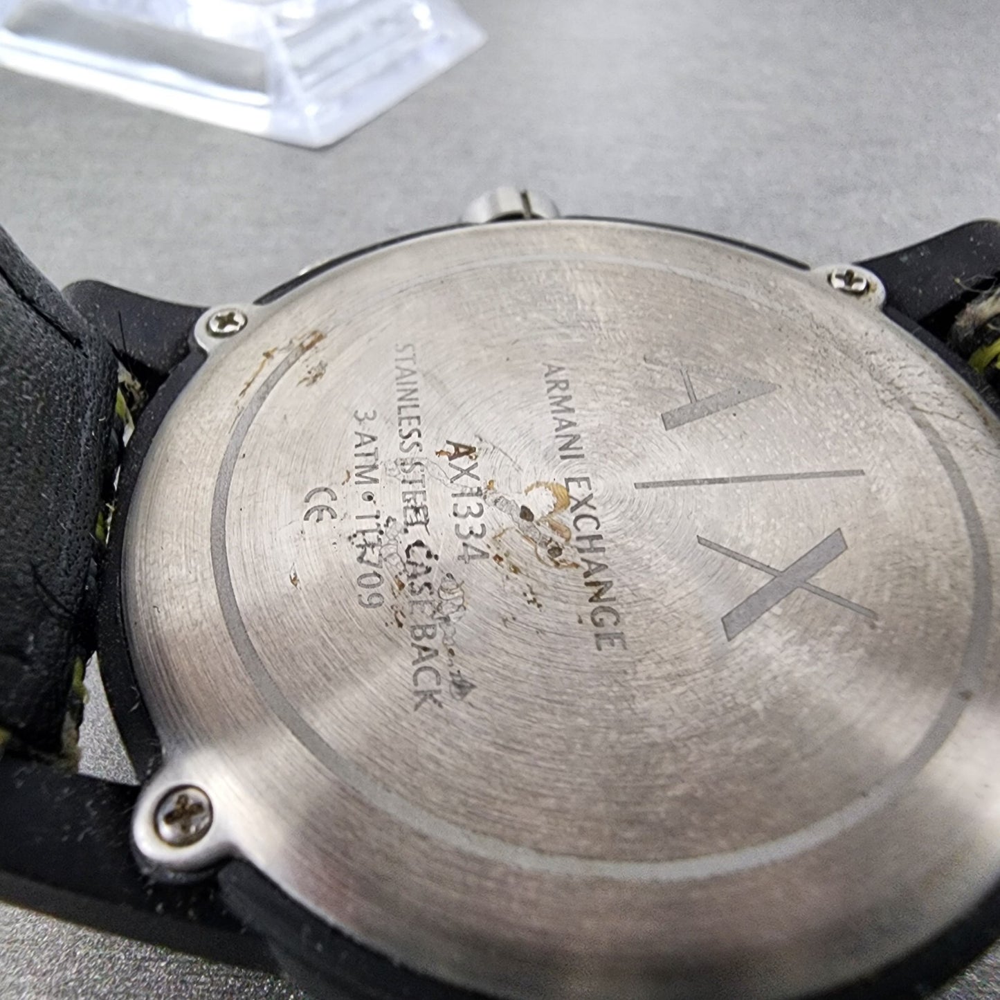 Close-up of worn Armani Exchange AX1334 stainless steel watch case back on gray surface.
