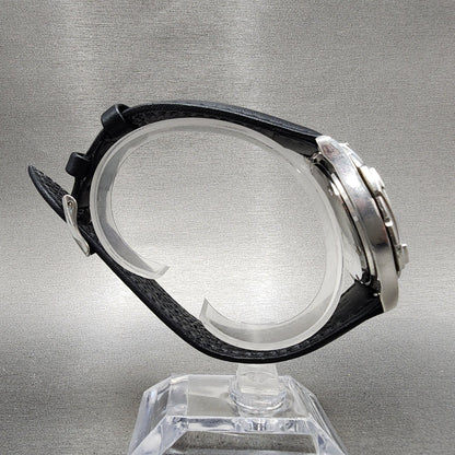 Side view of a silver wristwatch with black leather strap on a clear display stand