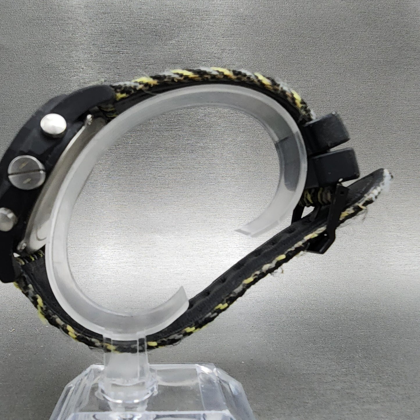 Side view of black digital watch with fabric band on display stand, gray background