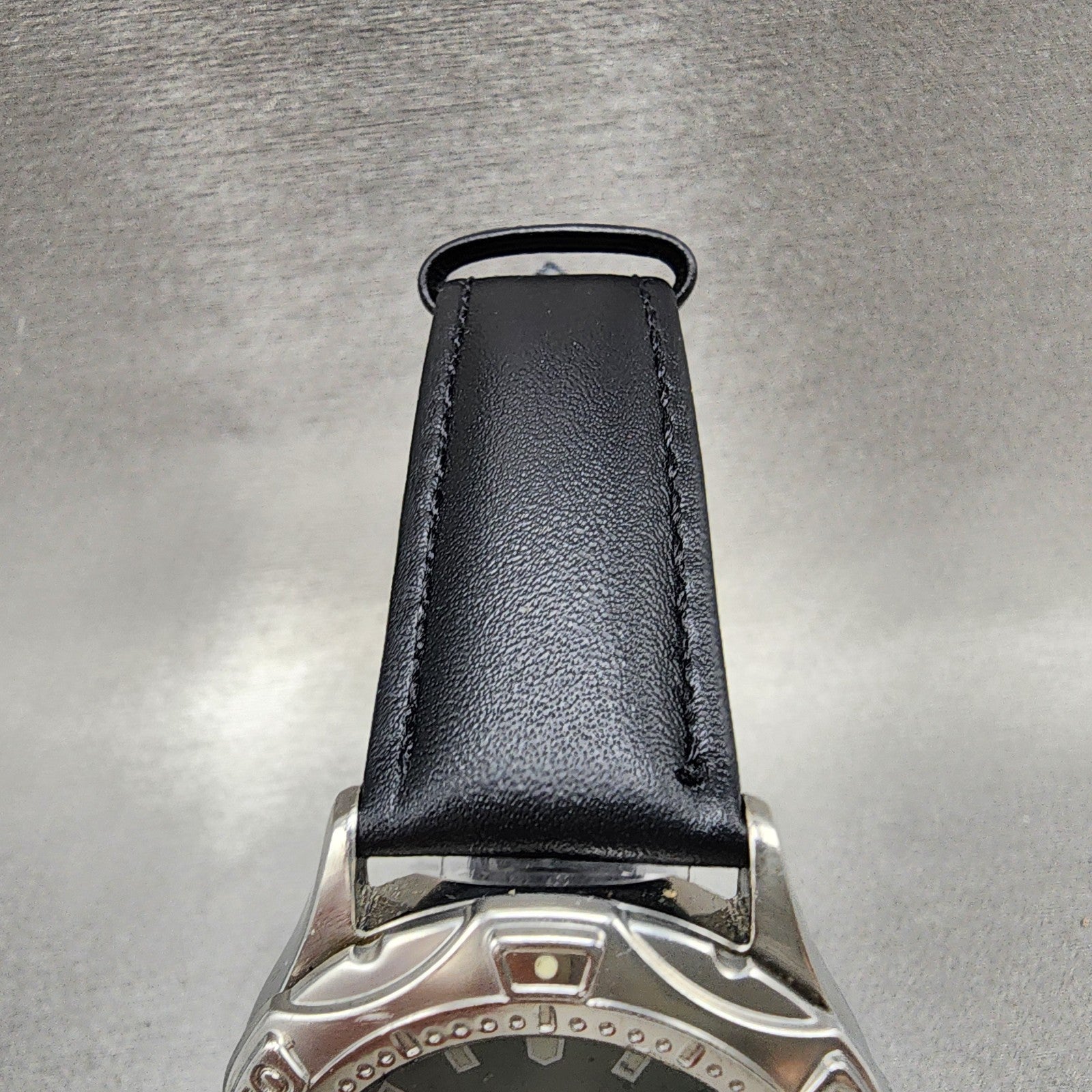 Black leather watch strap with stainless steel case on metallic background