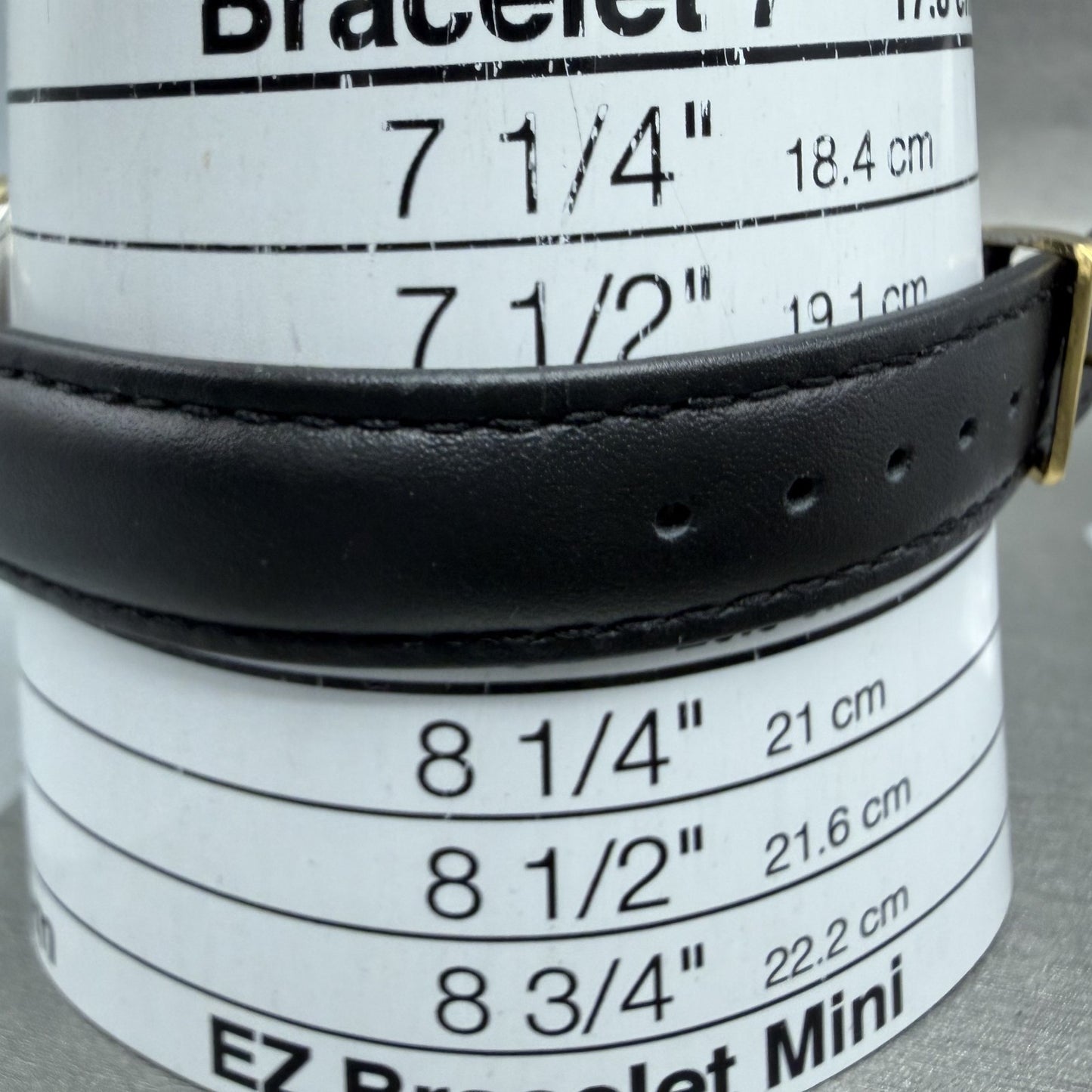 Black leather bracelet on size measuring tool with bracelet sizes in inches and centimeters.