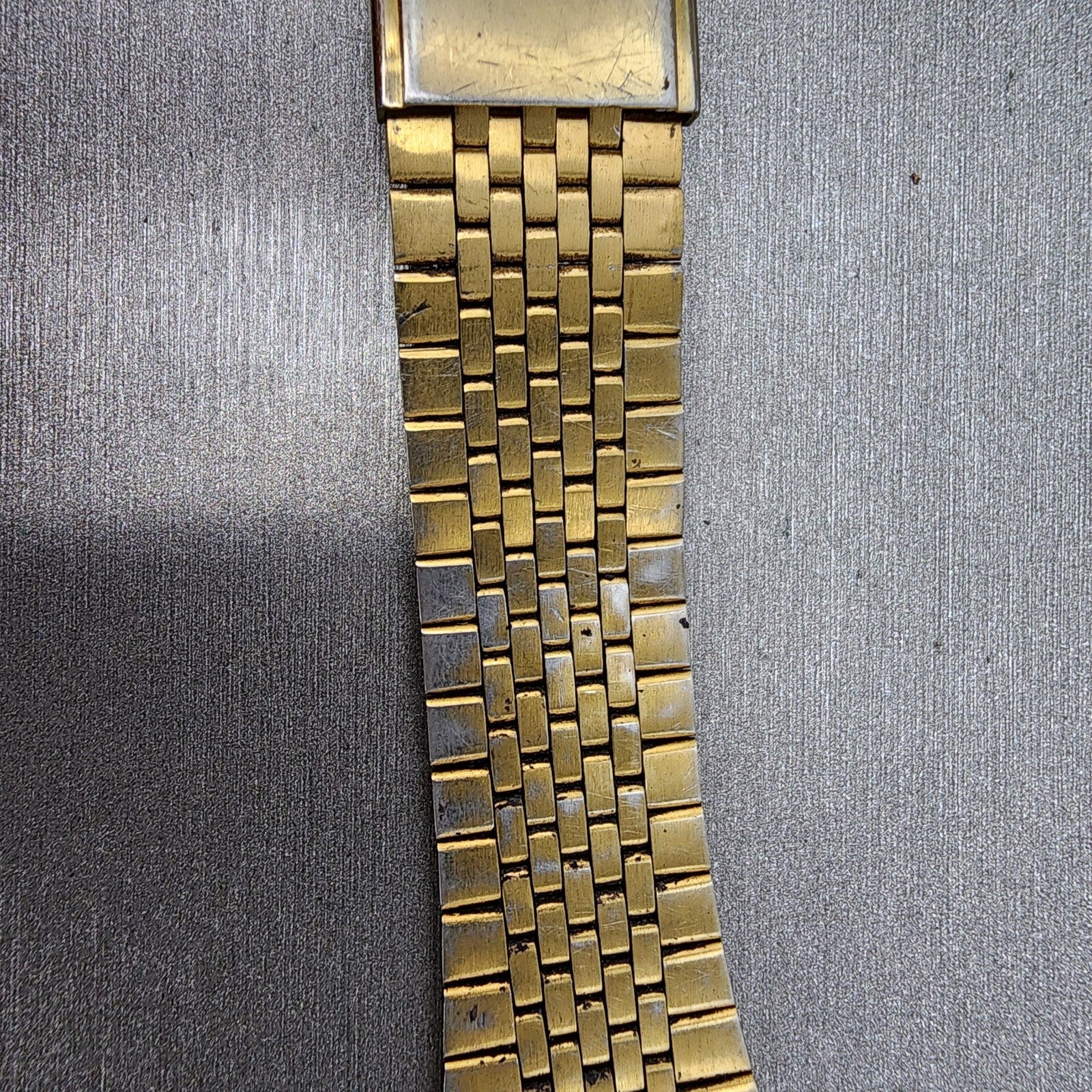 Close-up of vintage gold metal watch band with textured links on a gray surface