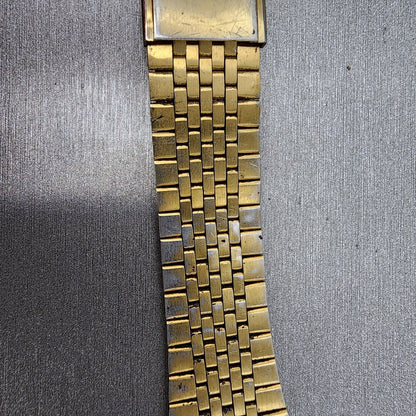 Close-up of vintage gold metal watch band with textured links on a gray surface