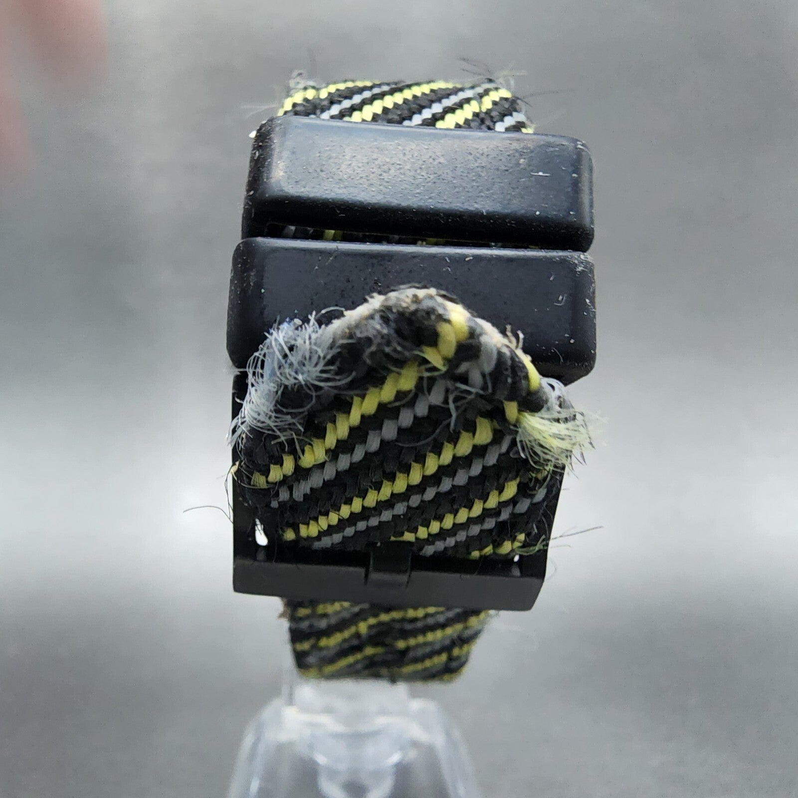 Frayed black, yellow, and gray striped nylon watch strap with black buckle on display.