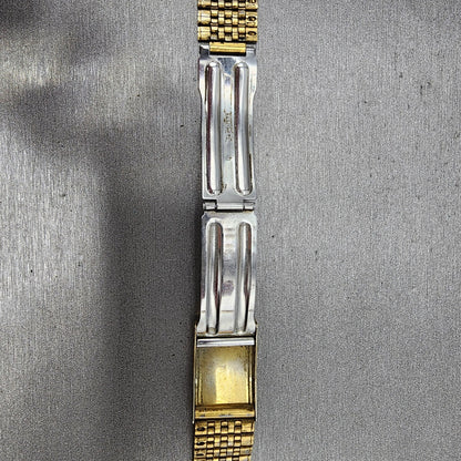 Two-tone metal watch band clasp on a textured gray surface