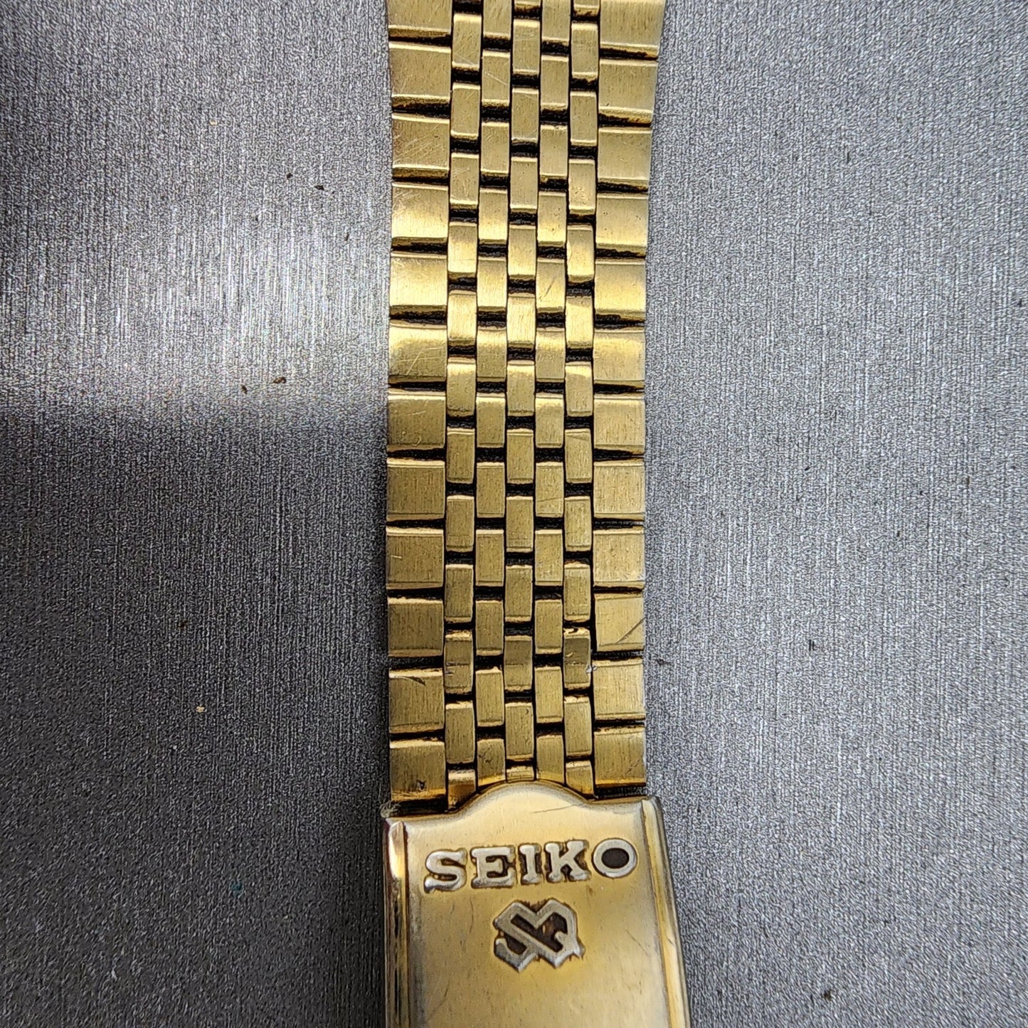 Seiko gold metal watch band with clasp on brushed silver background