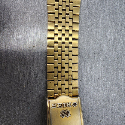 Seiko gold metal watch band with clasp on brushed silver background