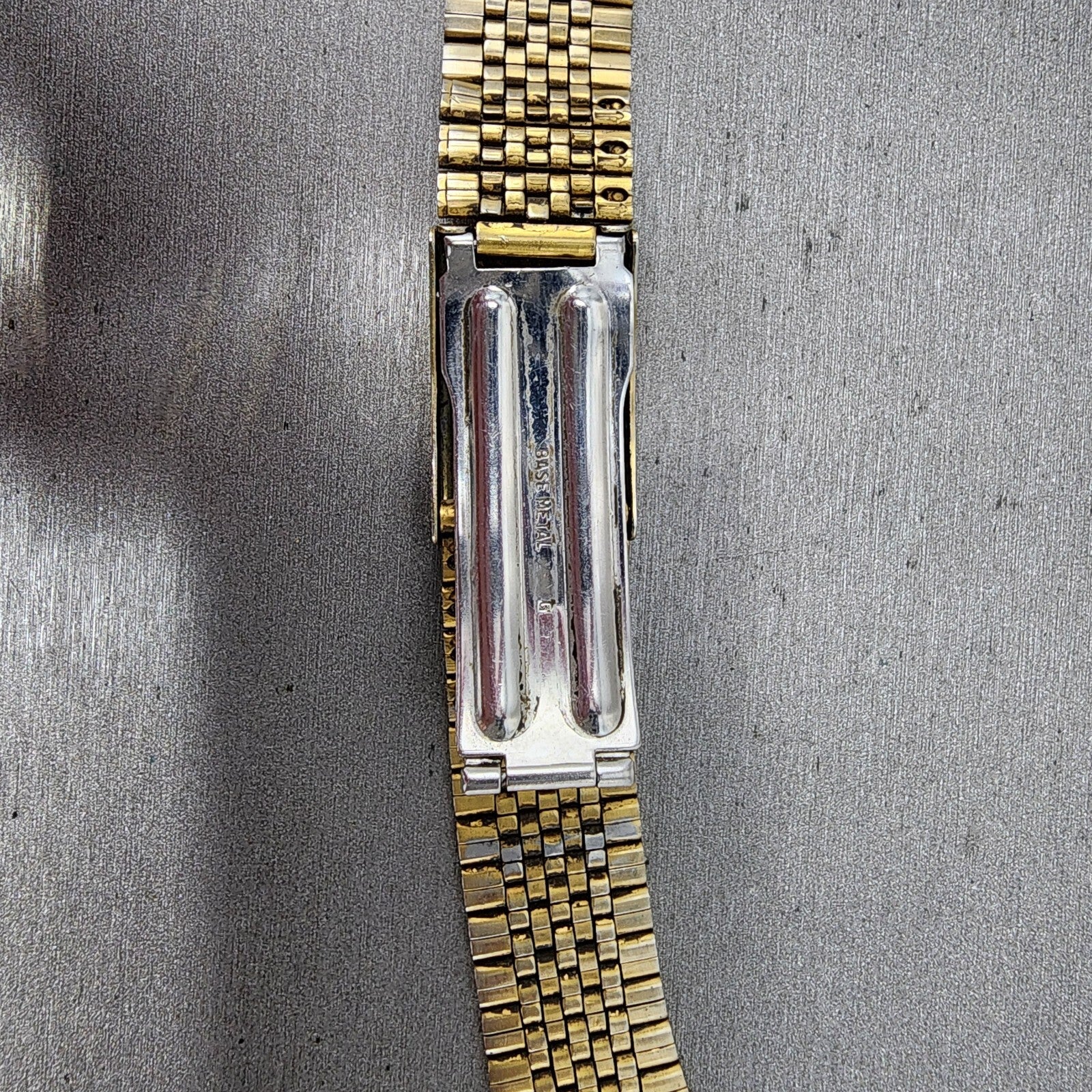 Close-up of gold metal watch band with silver clasp on textured gray background