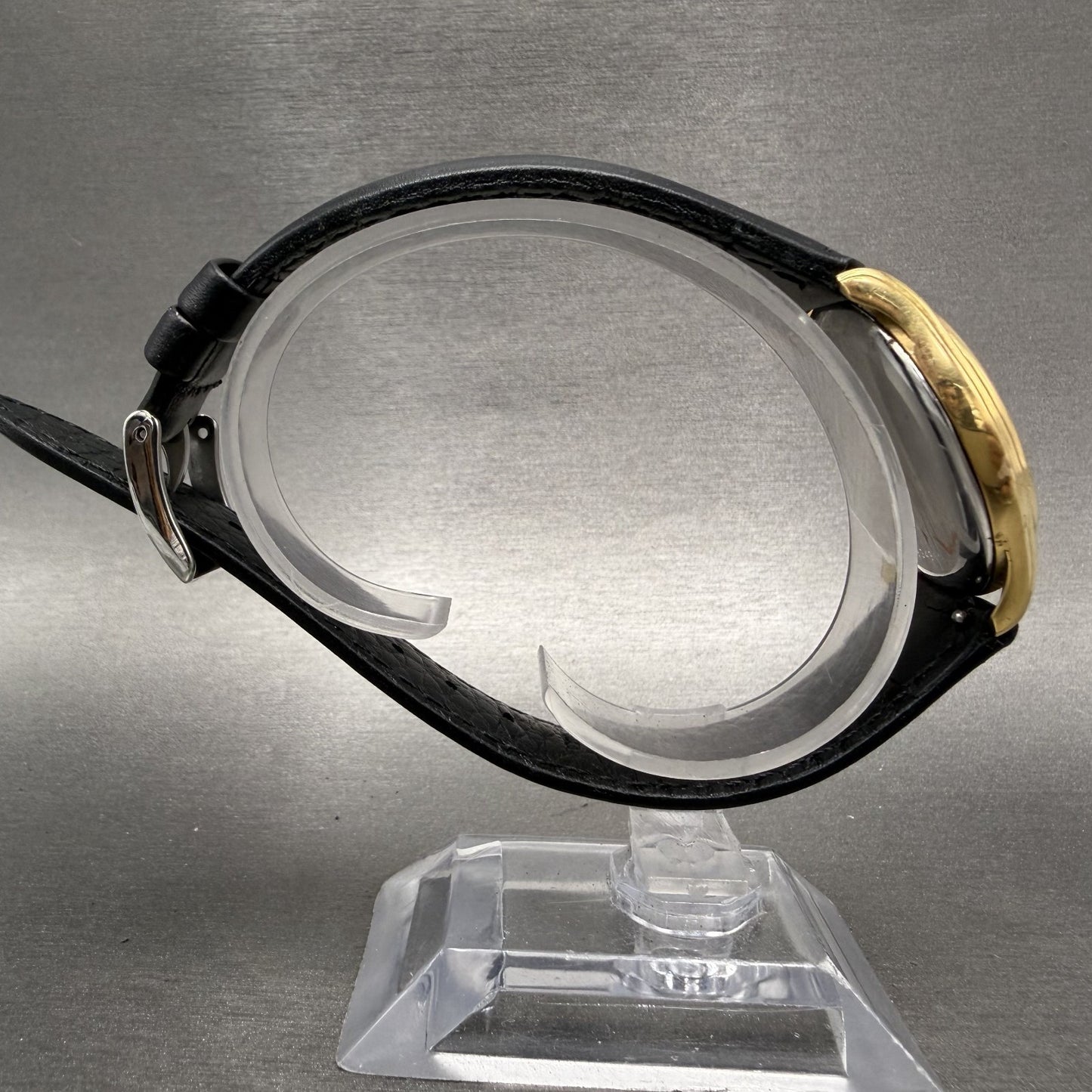 Side view gold watch case with black leather band on display stand
