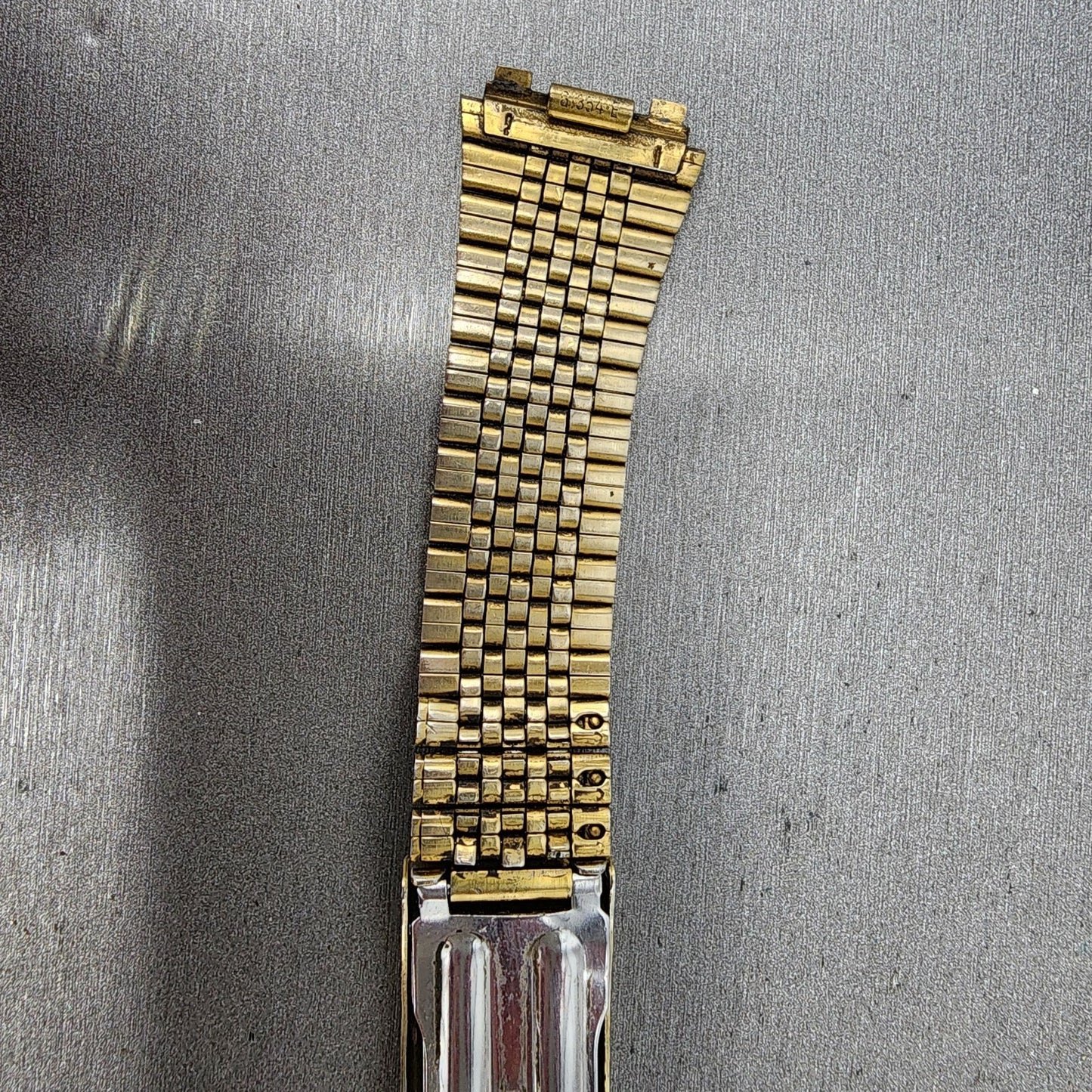 Close-up of vintage gold metal watch band with textured links on a gray background
