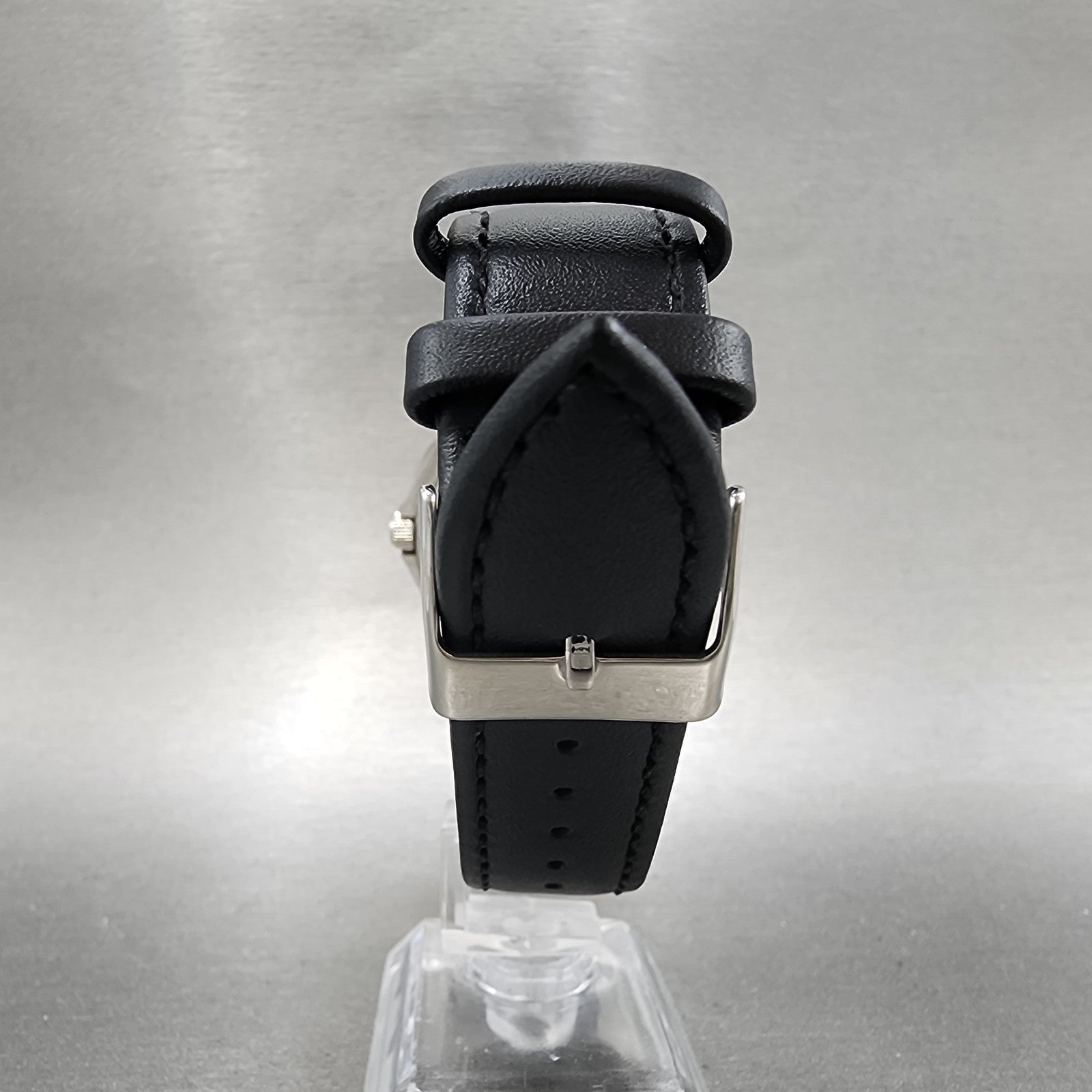 Black leather watch strap with silver buckle on display stand, grey background