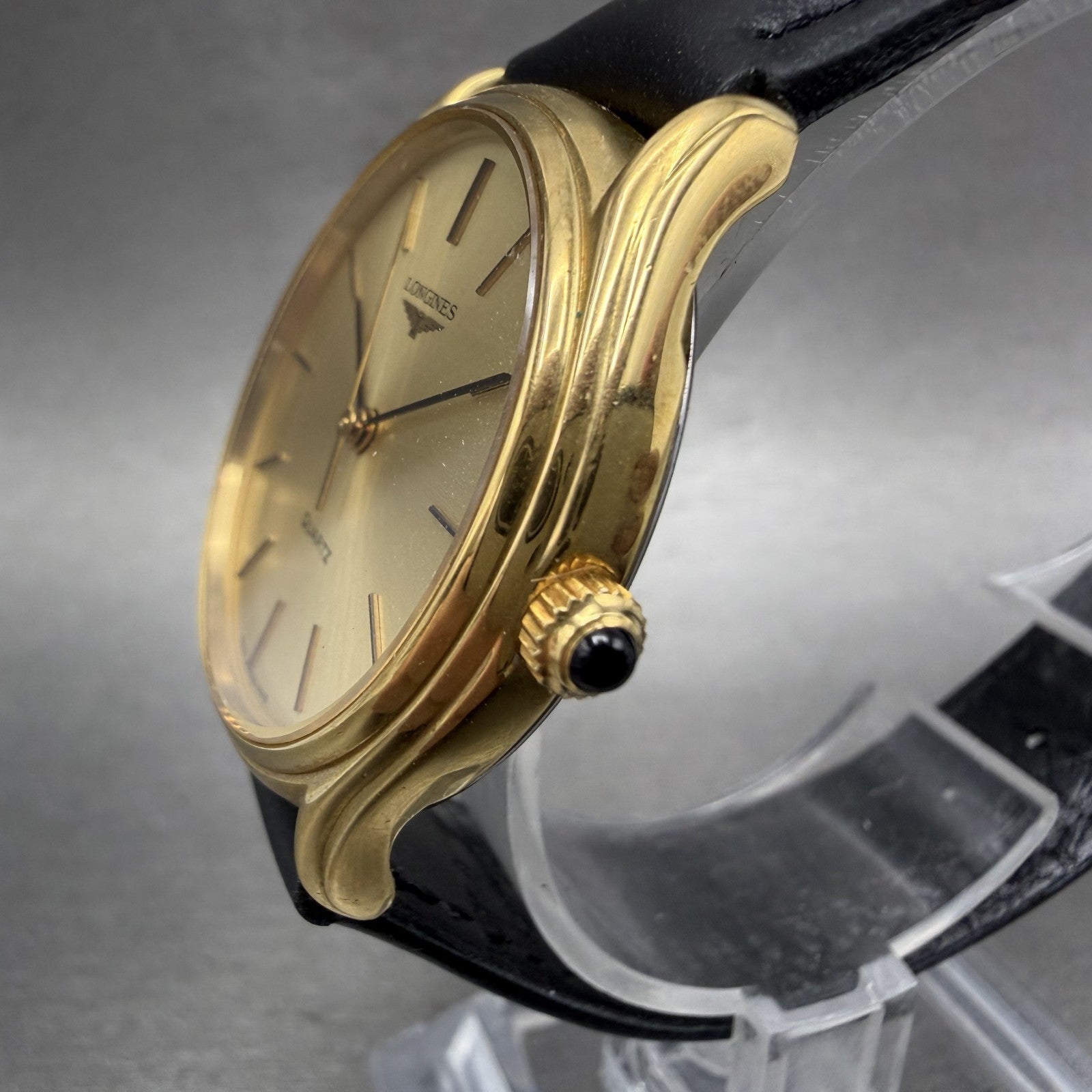 Gold Longines quartz wristwatch with black leather strap on display stand