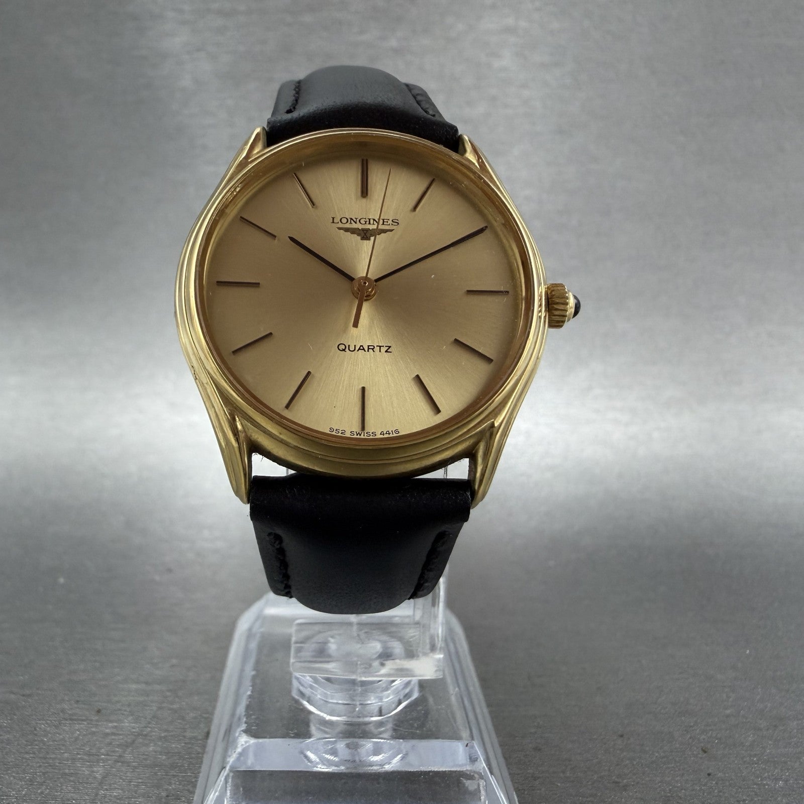 Vintage Longines gold quartz watch with black leather strap on display stand