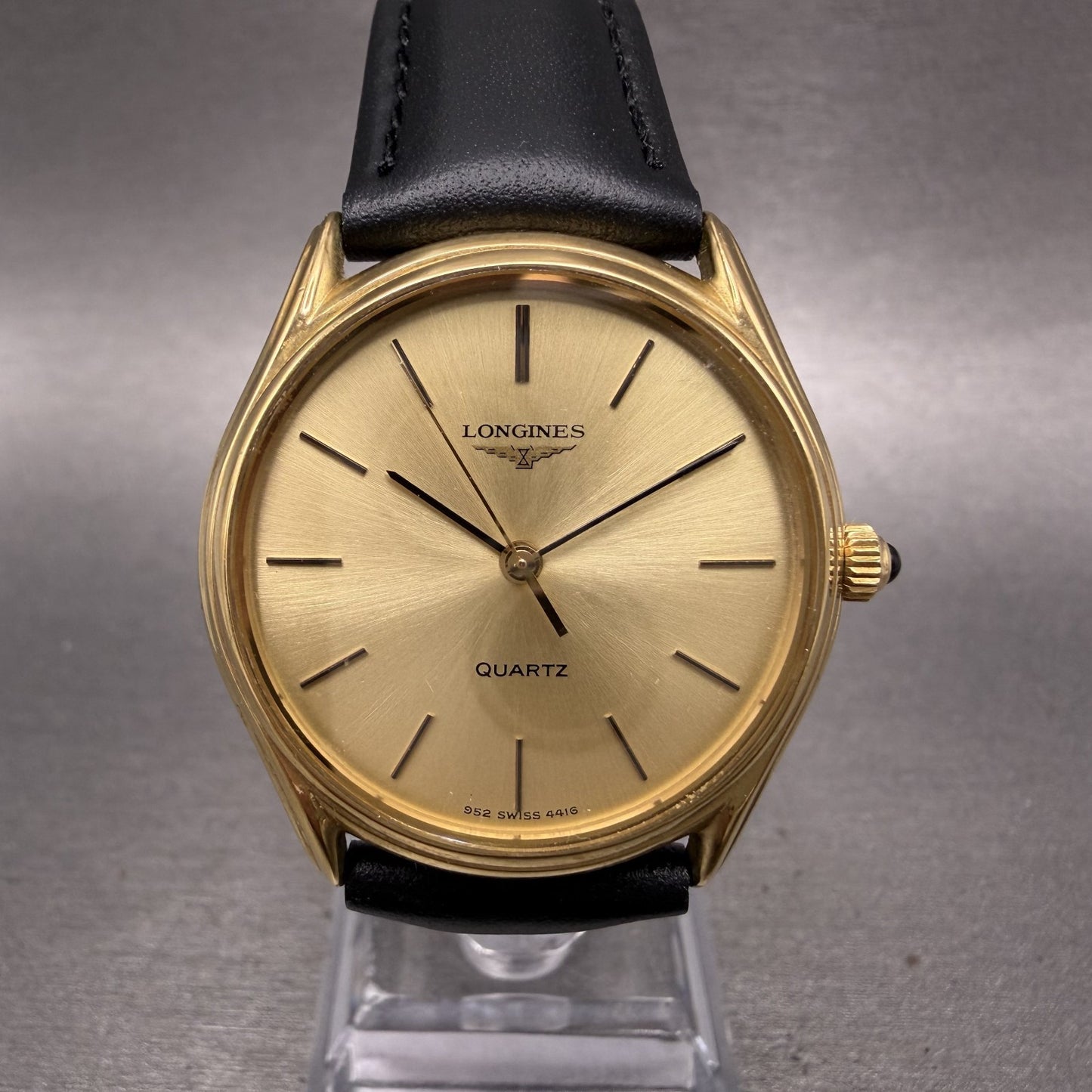Longines gold quartz watch with black leather strap on gray background
