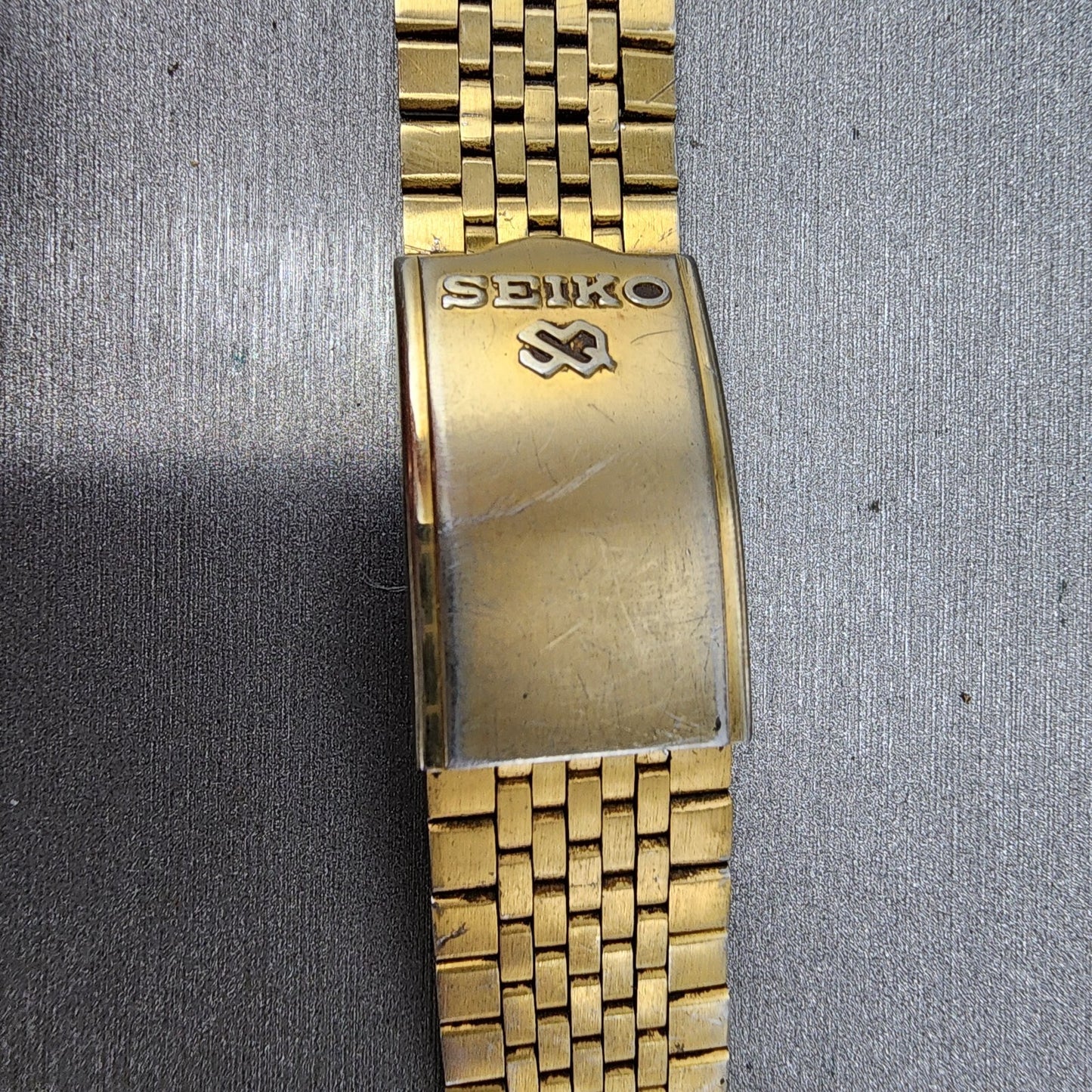 Vintage gold Seiko metal watch band clasp with Seiko logo on textured background