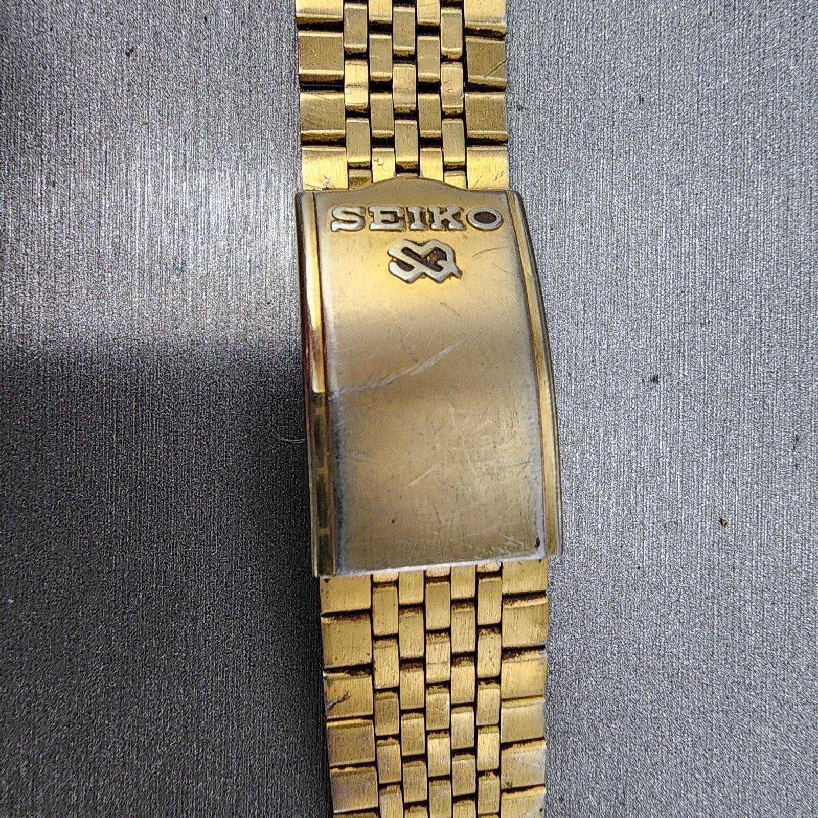Vintage gold Seiko metal watch band clasp with Seiko logo on textured background