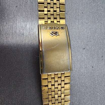 Vintage gold Seiko metal watch band clasp with Seiko logo on textured background