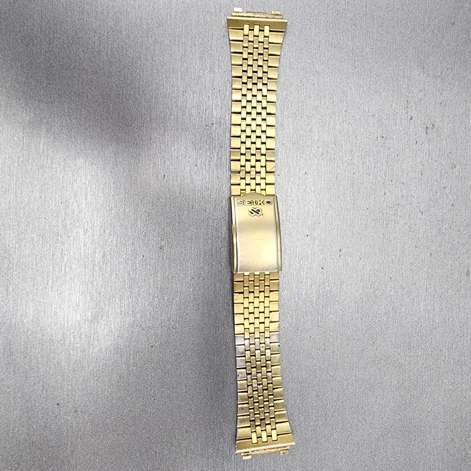 Seiko gold metal watch band with fold clasp on gray textured background