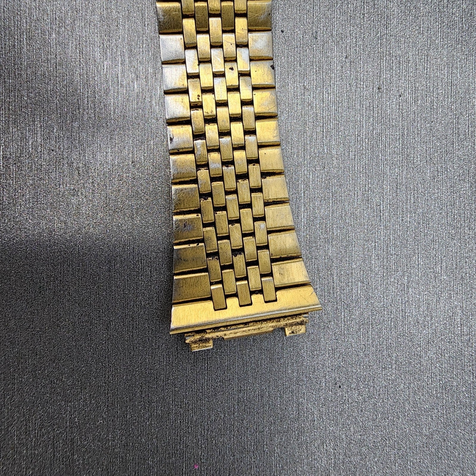 Close-up of a gold metal watch band on a textured gray surface