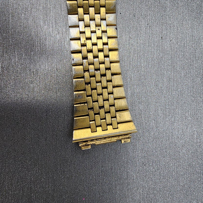 Close-up of a gold metal watch band on a textured gray surface