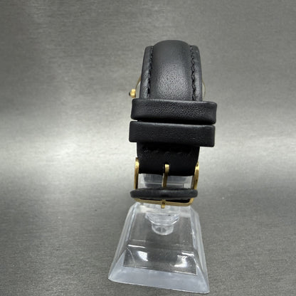Black leather watch strap with gold buckle on display stand against grey background
