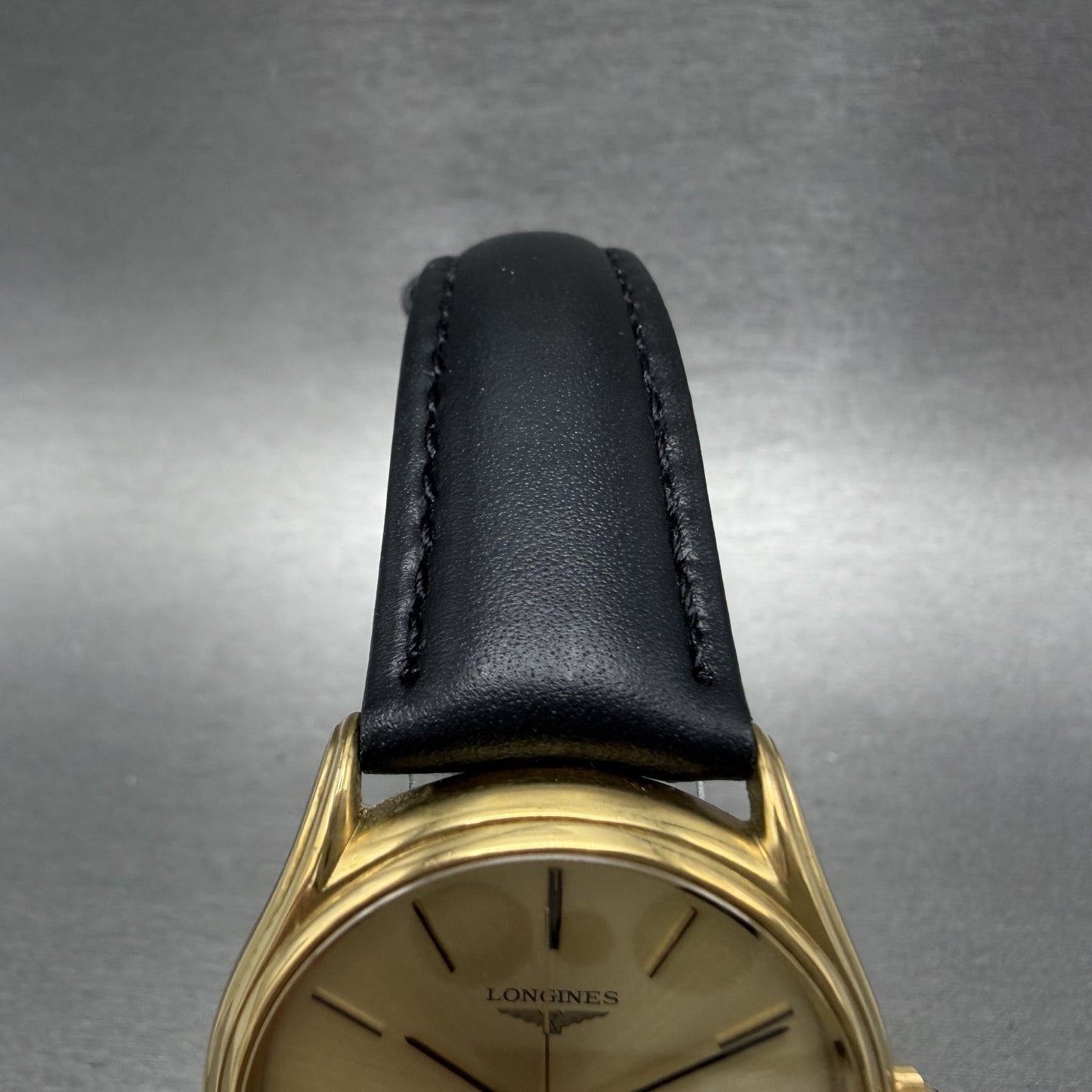 Longines gold watch with black leather strap on gray background