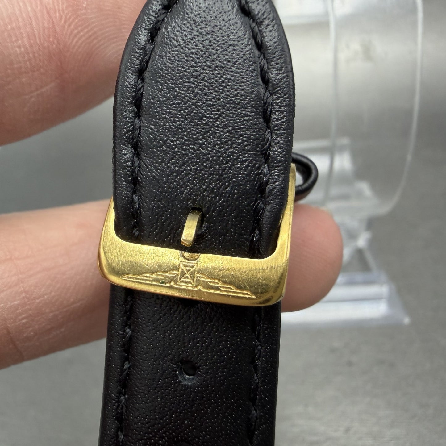 Gold buckle with engraving on black leather watch strap, close-up detail