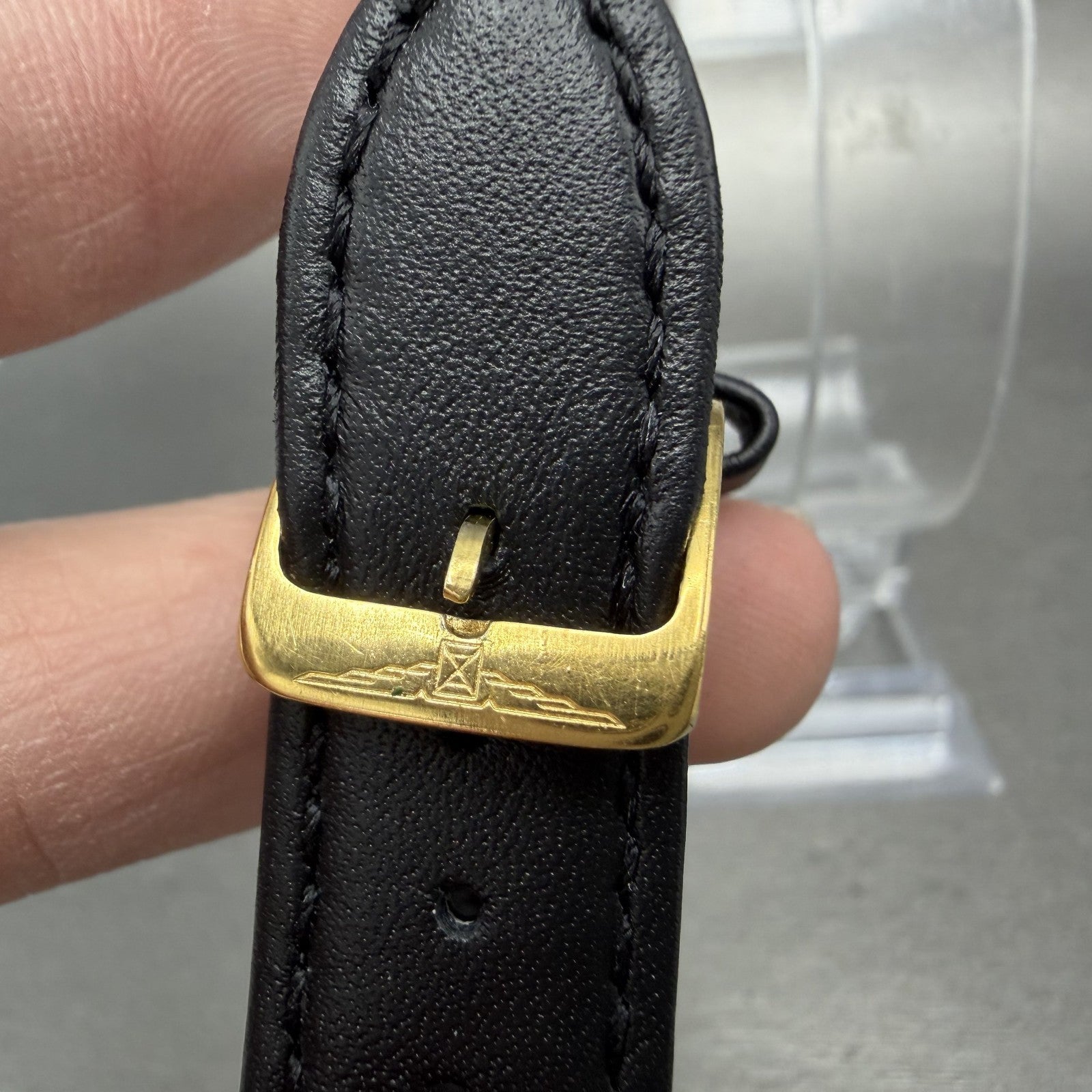 Gold buckle with engraving on black leather watch strap, close-up detail