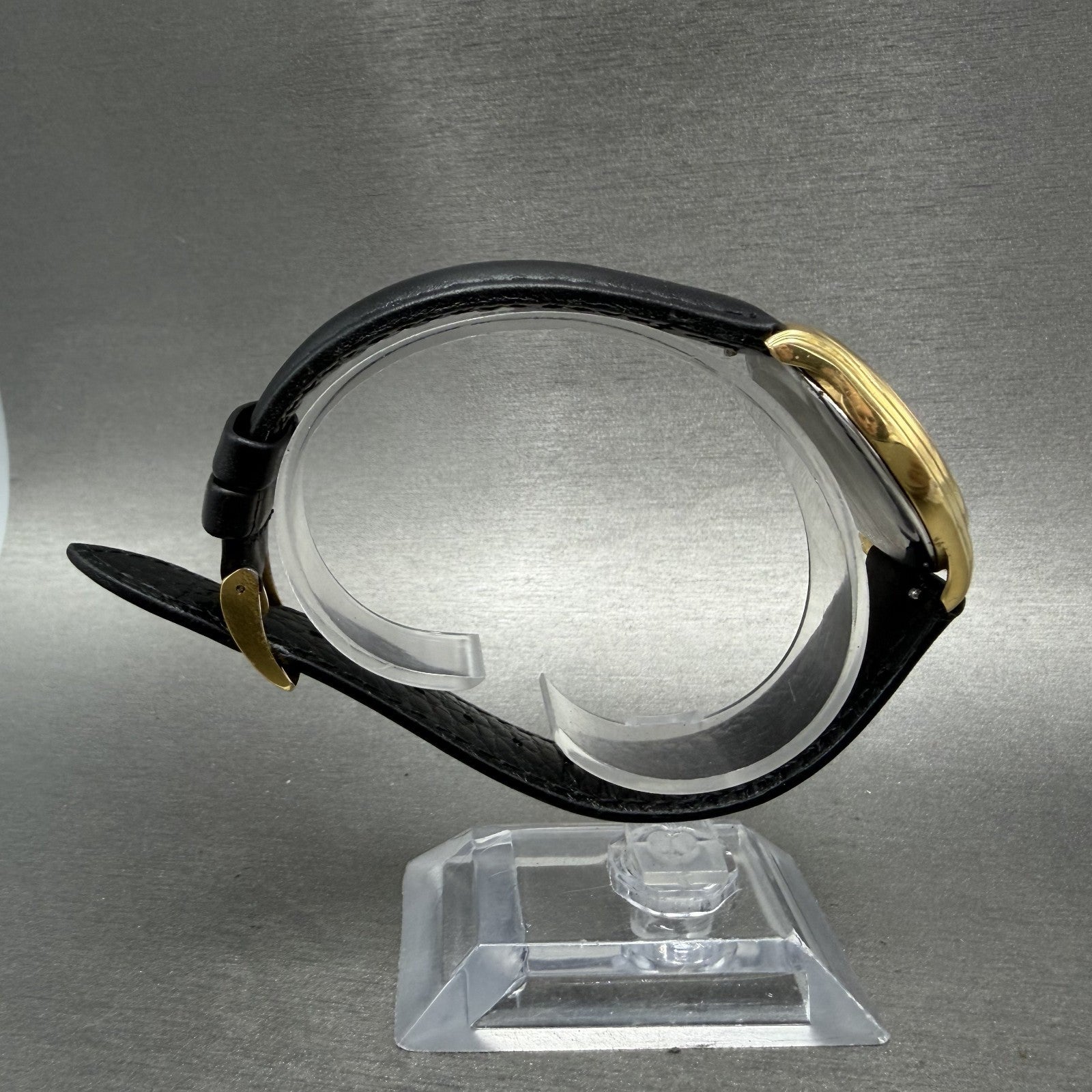 Gold wristwatch with black leather strap on display stand, side profile view