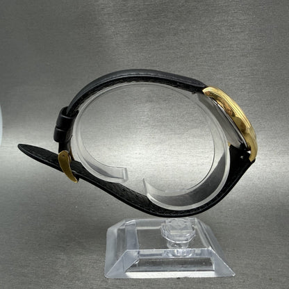 Gold wristwatch with black leather strap on display stand, side profile view