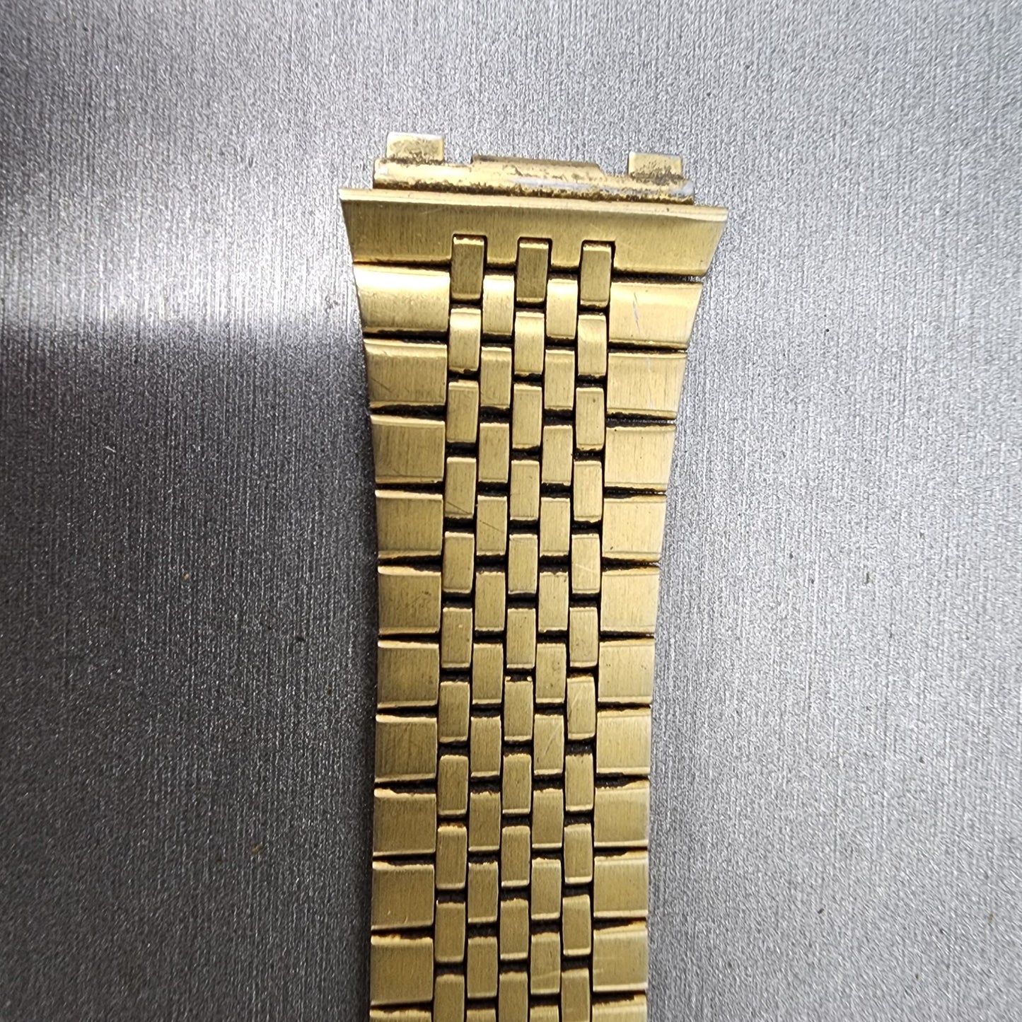 Close-up of a gold metal watch band on a gray textured background