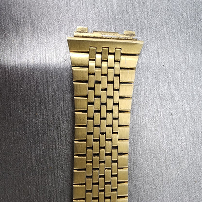 Close-up of a gold metal watch band on a gray textured background
