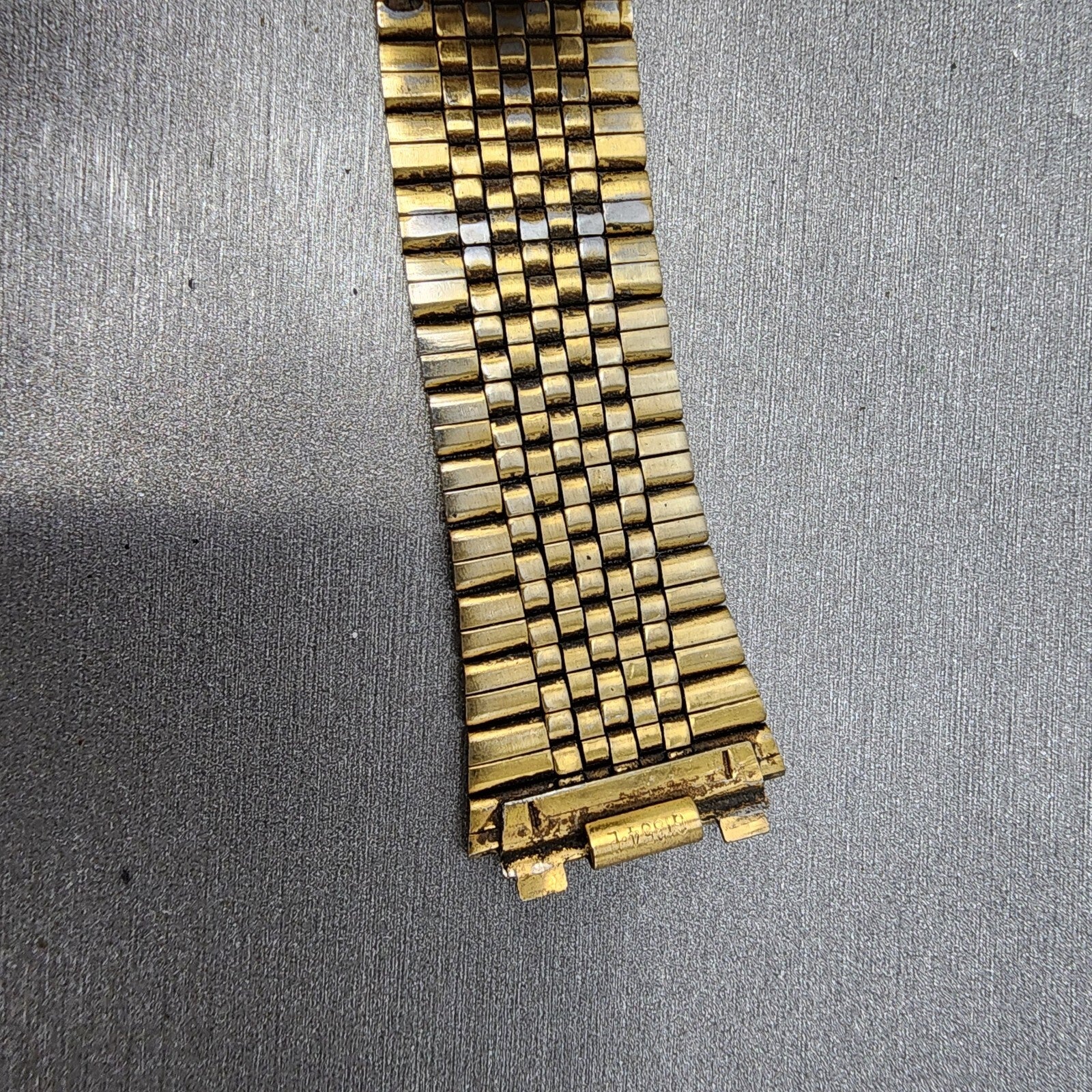 Vintage gold metal watch band with rectangular links on a textured gray surface